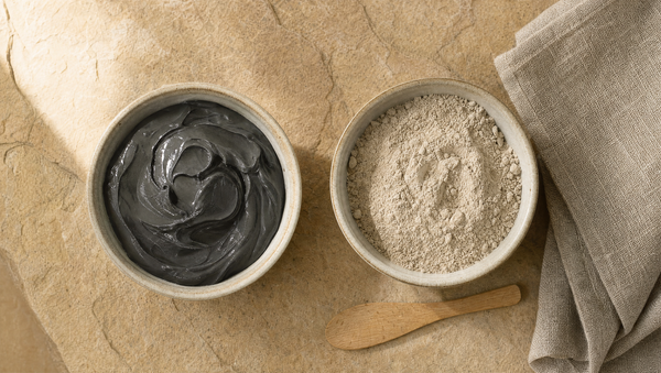 Two bowls side by side: dark Dead Sea mud and pale kaolin clay powder