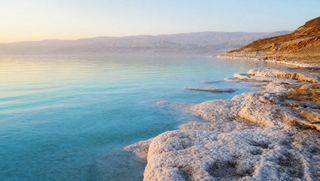 The Jordanian shore of the Dead Sea at golden hour with salt-crusted rocks