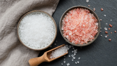 Two bowls side by side: white Dead Sea salt crystals and pink Himalayan salt