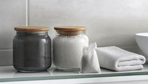 Sealed jars of Dead Sea mud and bath salt with wooden lids on a bathroom shelf