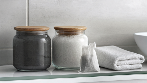 Sealed jars of Dead Sea mud and bath salt with wooden lids on a bathroom shelf